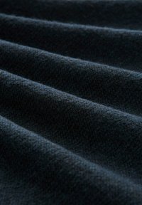 Tissu bleu marine drapé en plis doux et texturés ; le matériau paraît chaud et épais avec un tissage fin, affichant des variations subtiles de teinte.