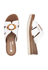 White slide sandals with cut-out design, tortoiseshell accent, and brown cushioned footbed. Thick, ridged sole for added comfort.