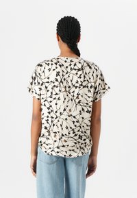 Kortermet bluse i kremfarge med svart blomsterdesign og brune detaljer. Har rund kant og avslappet passform, laget av lett stoff.