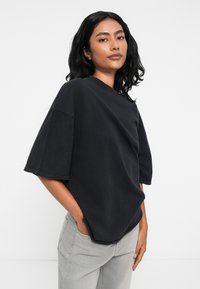 Μαύρη oversize μπλούζα με στρογγυλή λαιμόκοψη και κοντά μανίκια, κατασκευασμένη από μαλακό υλικό. Διαθέτει καμπυλωτό στρίφωμα και άνετη εφαρμογή.