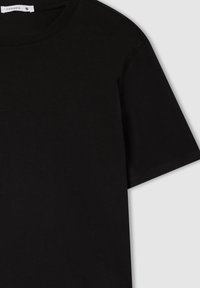 Czarny bawełniany t-shirt z okrągłym dekoltem, krótkimi rękawami i miękką teksturą. Posiada metkę na kołnierzyku wskazującą rozmiar.