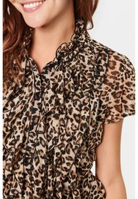 Bluse mit Leopardenmuster aus durchsichtigem Stoff, mit Rüschendetails an der Vorderseite, einem gewellten Ausschnitt und kurzen Puffärmeln. Schwarze Knöpfe sichtbar.