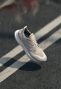 Vaaleanpunaiset urheilukengät, joissa on hengittävä verkkomateriaali, teksturoitu yksityiskohta, pehmustettu pohja ja nauhakiinnitys, esitetty tummalla taustalla.