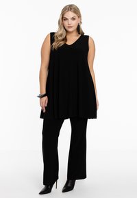 Schwarzes ärmelloses Tunika mit V-Ausschnitt, kombiniert mit weitgeschnittenen Hosen. Der Stoff ist glatt und das Outfit weist elegante Akzente auf.