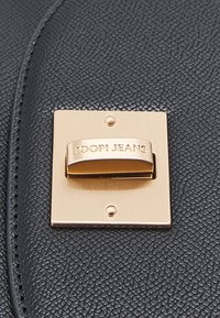 Chiusura rettangolare dorata con "JOOP! JEANS" inciso su una superficie in pelle nera testurizzata, fissata con due viti.
