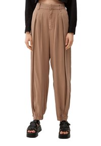 Lichtbruine, losse geplooide broeken met taps toelopende manchetten; gemaakt van een zachte stof. Gepaard met zwarte plateau-sandalen.