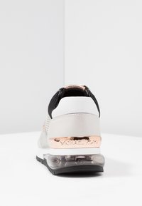 Szare sneakersy z czarną siateczką u góry, srebrnymi akcentami i przezroczystym obcasem. Posiadają logo w kolorze różowego złota na metalowym klipsie obcasa.