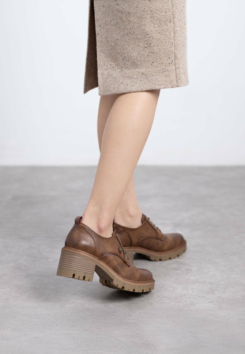 Zapatos de cuero marrón con cordones y suela de goma gruesa, con un tacón moderado, que presentan costuras en tono similar y un diseño de puntera redonda.