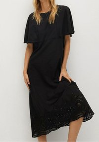 Schwarzes Kleid mit einem geschichteten Cape-Design, das bestickte Ausschnittdetails am Saum und eine lässige Silhouette bietet.