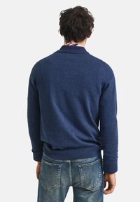Marineblauer gestrickter Pullover mit ribbeltem Kragen und Bündchen, kombiniert mit hellblauen Jeans. Der Pullover hat ein klassisches, körperbetontes Design.