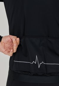 Schwarzes Radtrikot mit einem weißen Herzschlaglinien-Design. Das Material scheint leicht und elastisch zu sein, mit einer körperbetonten Passform und einer Rückentasche.