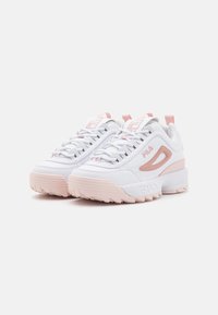 White athletic shoes with pink accents, featuring a textured upper, thick sole, and sturdy laces. Notable side logo detail and pull tab.