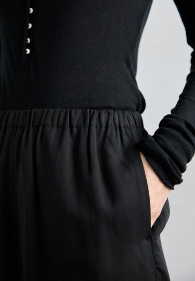 Black long-sleeve top with button detail, paired with black pants featuring an elastic waistband and side pockets. Smooth, soft texture.