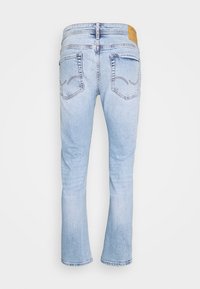 Calças de ganga de um azul claro com um design flare, apresentando dois bolsos traseiros e uma textura ligeiramente desbotada. Um retângulo de pele castanha é visível na parte de trás da cintura.