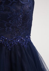 Mörkblå klänning med spetsliv, broderade blommönster med pärlor och en tyllkjol. Detaljerad textur och mönster synliga.