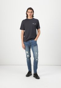 Mørkegrå kortermet t-skjorte med et lite hvitt grafisk trykk, før det er kombinert med lyseblå slitte slim-fit jeans og svarte snørebåndsko.