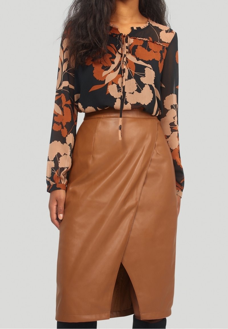 Kvinna iklädd en brun faux läder omslagskjol och en svart blus med stora beige och rostfärgade blommönster.