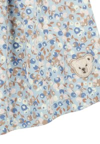 Tessuto azzurro chiaro con un motivo floreale in blu, rosa e marrone. Presenta una toppa a ricamo a forma di orso sul lato inferiore destro. Tessuto morbido.