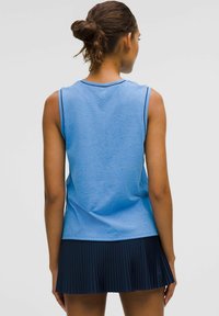 Maglietta atletica blu senza maniche realizzata in tessuto liscio, abbinata a una gonna a pieghe blu navy. La maglietta ha un collo rotondo e cuciture sottili.