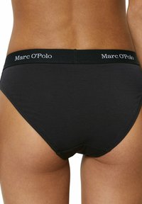 Zwarte katoenen slips met een gladde textuur, uitgerust met een brede elastische tailleband met het merk "Marc O’Polo" in witte letters.