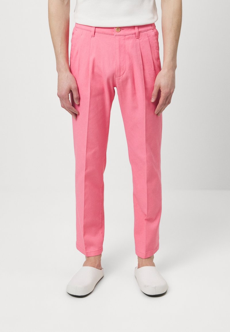 Różowe bawełniane spodnie o prostym kroju, z dwoma plisami z przodu i zapięciem na guzik. W połączeniu z białym obuwiem wsuwanym.