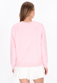 Sudadera rosa claro con mangas raglán y puños acanalados. Presenta un diseño sencillo, combinada con una falda blanca plisada.