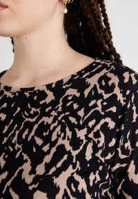 Svart och beige topp med leopardmönster, rund halsringning och mjuk textur. Detalj på halsringningen synlig, vilket framhäver tyget.