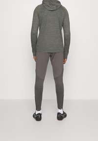 Veste à capuche grise et pantalon gris ajusté avec des accents texturés, chaussures de sport noires, leggings bicolores et zippers aux chevilles.