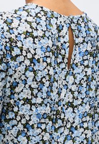 Blouse à motif floral avec de petites fleurs bleues, blanches et vertes sur tissu noir, avec une fermeture bouton goutte d'eau dans le haut du dos.