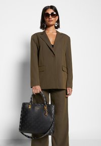 Černá kabelka s monogramem a zlatými detaily, s texturovanými akcenty. Strukturovaný tvar s dvojitými ušima a odnímatelným popruhem.