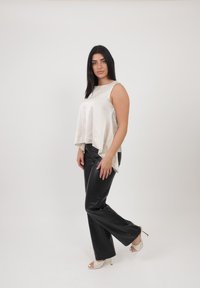 Top senza maniche in satin beige chiaro con orlo asimmetrico, abbinato a pantaloni neri in similpelle a vita alta e tacchi bianchi aperti.