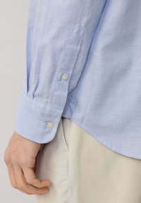 Camisa a cuadros azul claro con puños abotonados. La tela parece ser un material transpirable con una textura suave.