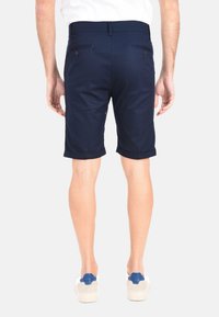 Pantaloni corti blu navy con una texture liscia, orlo ripiegato e tasche posteriori. Indossati con sneakers bianche con accenti blu.