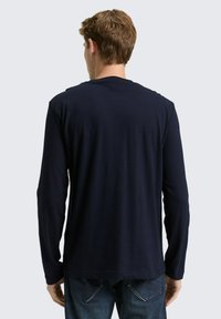 Granatowa koszula z długim rękawem wykonana z miękkiego materiału, z okrągłym dekoltem i prostym dołem. Widoczne przeszycia i dopasowany krój; noszona z ciemnymi dżinsami.