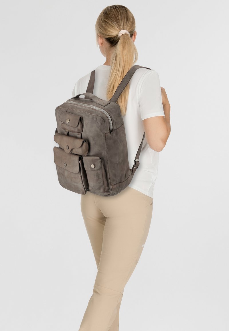 Zaino in pelle grigia con più tasche frontali, chiusura con zip e spallacci regolabili, che presenta una finitura texturizzata e un design minimalista.