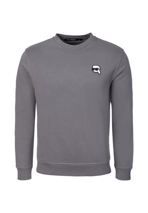 Šedá mikina s dlouhým rukávem a kulatým výstřihem, s malou nášivkou karikatury obličeje s brýlemi na slunce na levé straně hrudi.