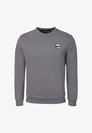 Šedá mikina s dlouhým rukávem a kulatým výstřihem, s malou nášivkou karikatury obličeje s brýlemi na slunce na levé straně hrudi.