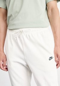Spodnie dresowe Nike w kolorze białym, z elastycznym paskiem w talii i sznurkiem oraz małym czarnym logo na lewej nogawce. Wykonane z miękkiego materiału bawełnianego.