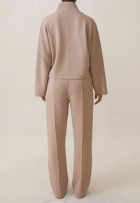 Jasnobeżowy zestaw odzieży domowej z kołnierzykiem i luźnym krojem. Góra ma prosty krój, natomiast spodnie mają zwężane nogawki i detale szwów.