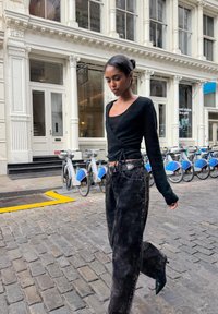 Černý svetřík s dlouhými rukávy, kombinovaný s volně střiženými černými džínami s efektem vyblednutí. Modelka má na sobě špičaté černé podpatky a stojí na dlážděné ulici.