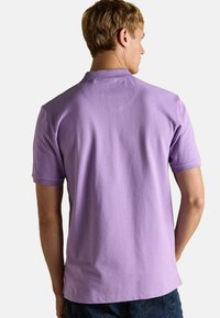 Īsām piedurknēm, ar apkakli veidota polo kreklu lavandas krāsā ar gludu tekstūru, kas iekļauj muguras vīli un sānu šķēlumus malā.