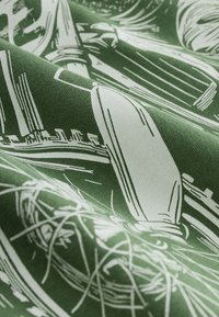 Tessuto verde con motivo astratto bianco composto da forme allungate, linee e trame. Il design presenta una finitura liscia, leggermente testurizzata.