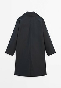 Zwarte jas met een puntkraag, lange raglanmouwen en een rechte snit. Het materiaal lijkt soepel met minimale naden en geen zichtbare hardware.