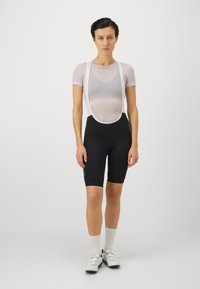 Schwarze Radsportshorts mit tailliertem Design, ausgestattet mit einem weißen Mesh-Träger und kurzen Ärmeln. Akzente setzen Knopfdetails an den Shorts.