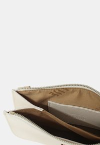 Pochette zip in pelle bianca con rivestimento in tessuto beige, dotata di più scomparti e una texture liscia. Zip con accessori metallici.