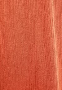 Tissu texturé de couleur corail atténuée, présentant une apparence légère et légèrement froissée avec de subtiles variations dans le motif de tissage.