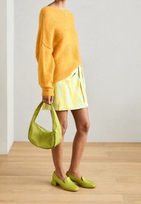 Suéter amarillo de peluche, falda azul claro y amarilla con estampado, bolso verde y mocasines verdes con tacones bajos y cuadrados.