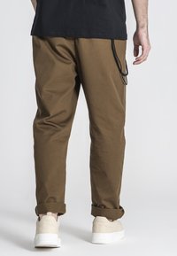 Bruine tapse broek van textuurstof, met een zwarte aantrekkoorddetail. Gedragen met opgerolde naden en witte sneakers.
