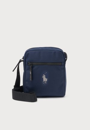 Marineblaue Umhängetasche mit schwarzem verstellbarem Riemen, frontaler Reißverschlusstasche und kleinem, grau besticktem Polospieler-Logo.