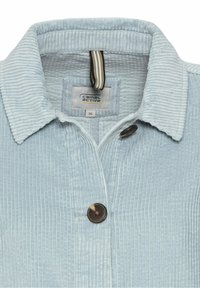 Chemise en velours côtelé bleu clair avec un col, deux boutons marron visibles, et une étiquette "camel active" à l'intérieur de l'encolure.